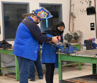 Male adult teaching female student how to weld