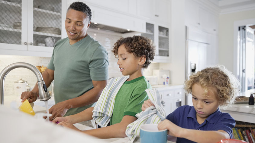 A man with two young boys washing and drying dishes