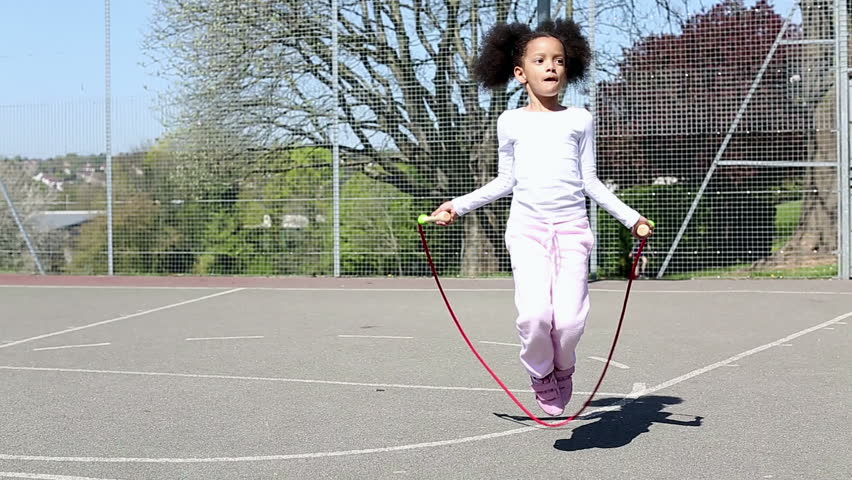 Young female girl skipping rope outside in a fenced in area