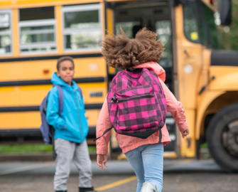 Student moving towards the bus while another student waits by the door