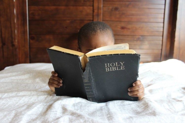 young child laying on a bed reading the bible