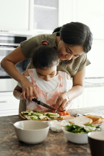 a mother helping her young daughter cut vegetables