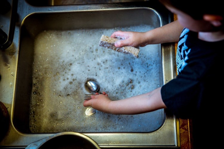 a young child washing a fork in the sink