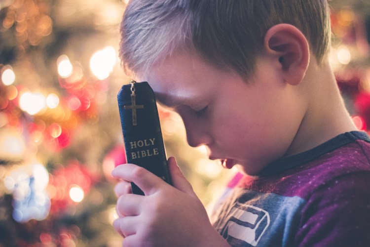 a young boy holding a bible praying
