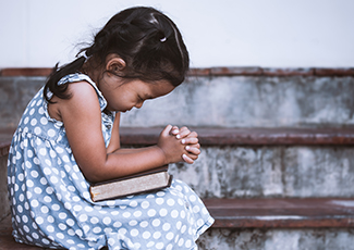 Photo of little girl praying with book in her hands