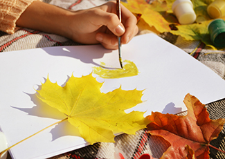 photo of a hand painting on paper with yellow and red leaves on top