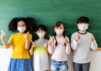 Male and female students standing beside each other wearing masks and giving thumbs up in a classroom