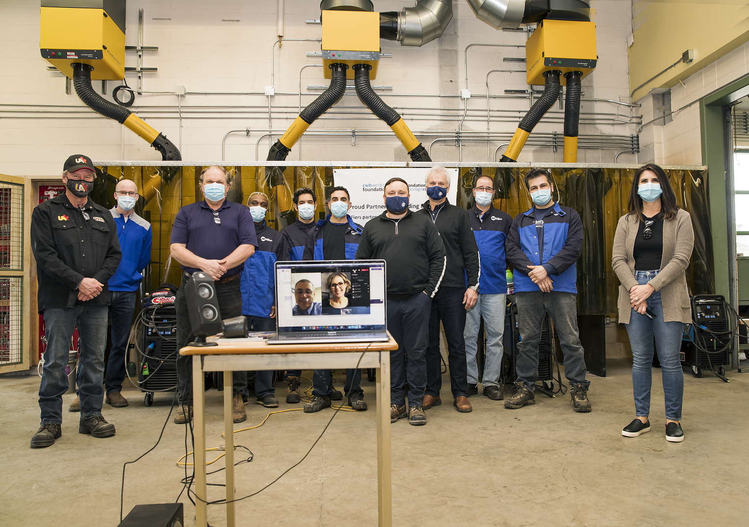 Male and female adults standing together social distanced and wearing masks in schools new welding booths technology classroom