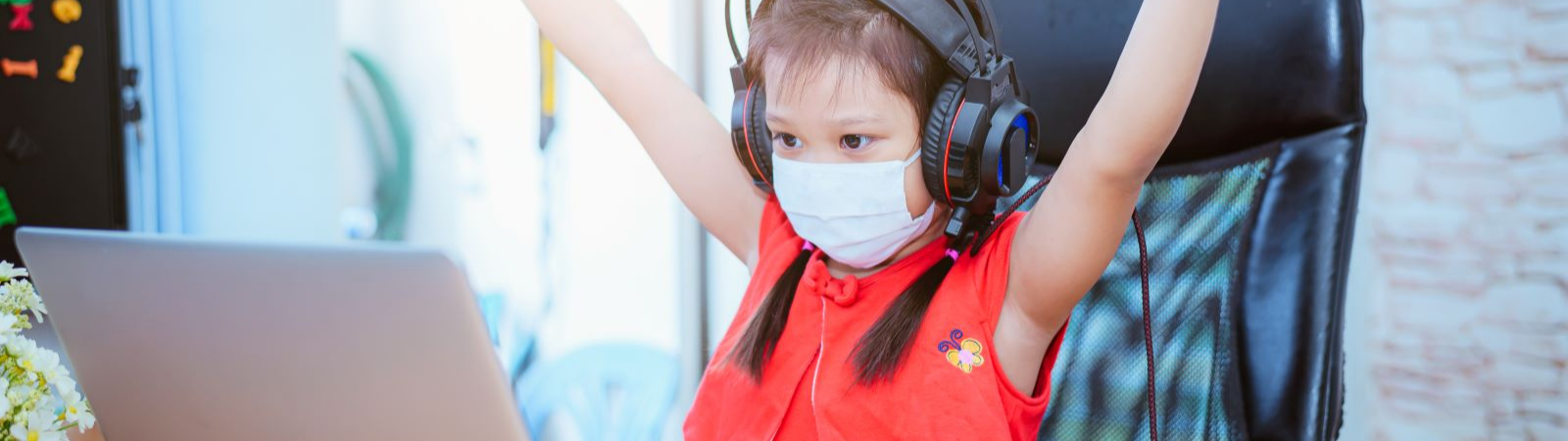 girl wearing a mask and head phones on a laptop with arms in the air