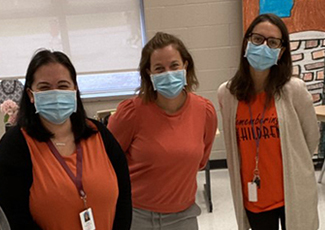 Three educators wearing orange shirts and medical masks in a school