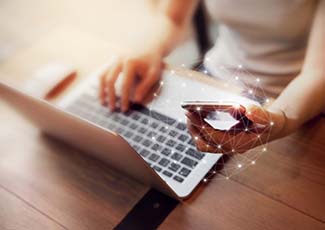 Person working on a laptop and holding a cellphone