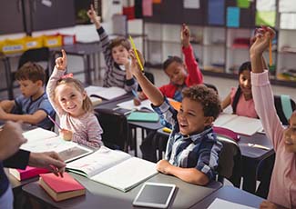 Group of young students with their hands up in a classroom