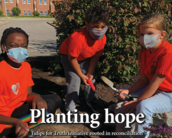 Students wearing orange shirts and masks and planting bulbs in a garden