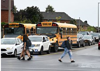 Buses in traffic and students walking across a street