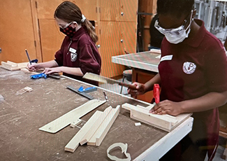 Secondary students cutting and sanding wood that will be made into crosses