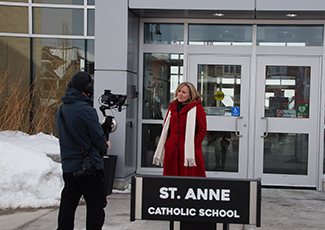 Female adult speaking on camera in front of St. Anne Catholic School