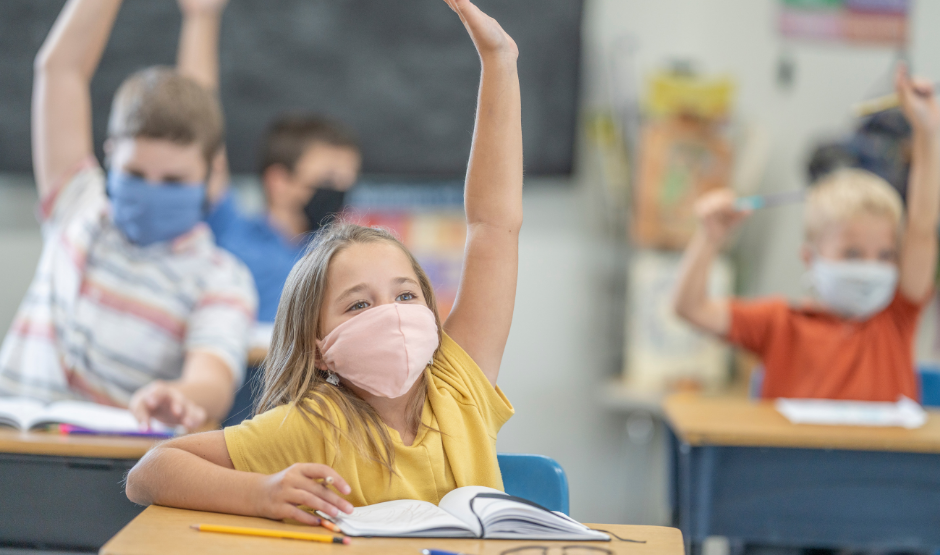 Students with masks in classroom raising their hands