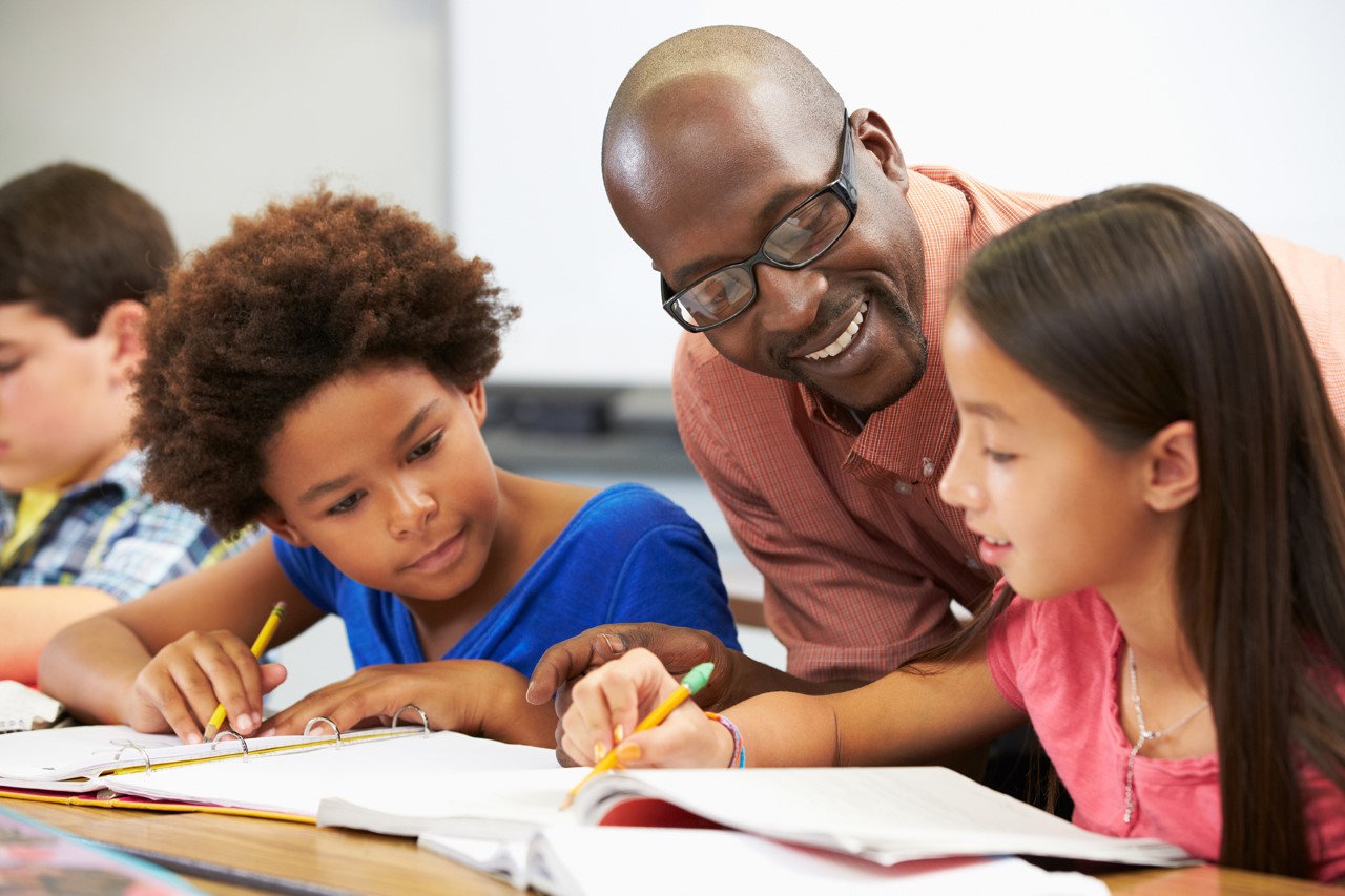 Male teacher talking with two female students in a classroom