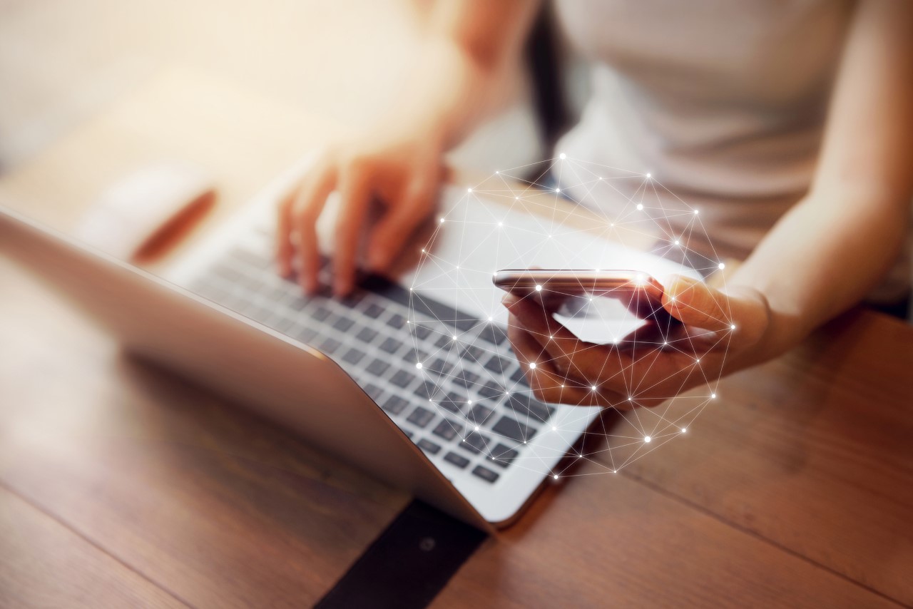 hand holding a cellphone and on a laptop at the same time