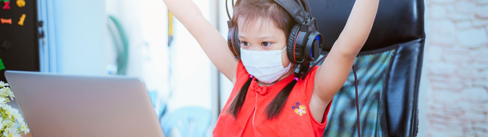 Female student wearing a mask and headphone with arms in the air