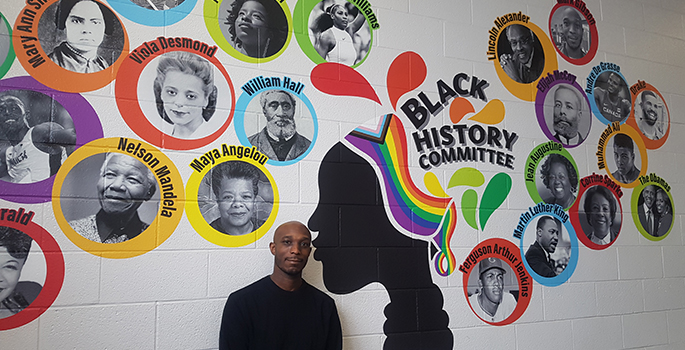 Male adult standing in front of Black Excellence mural
