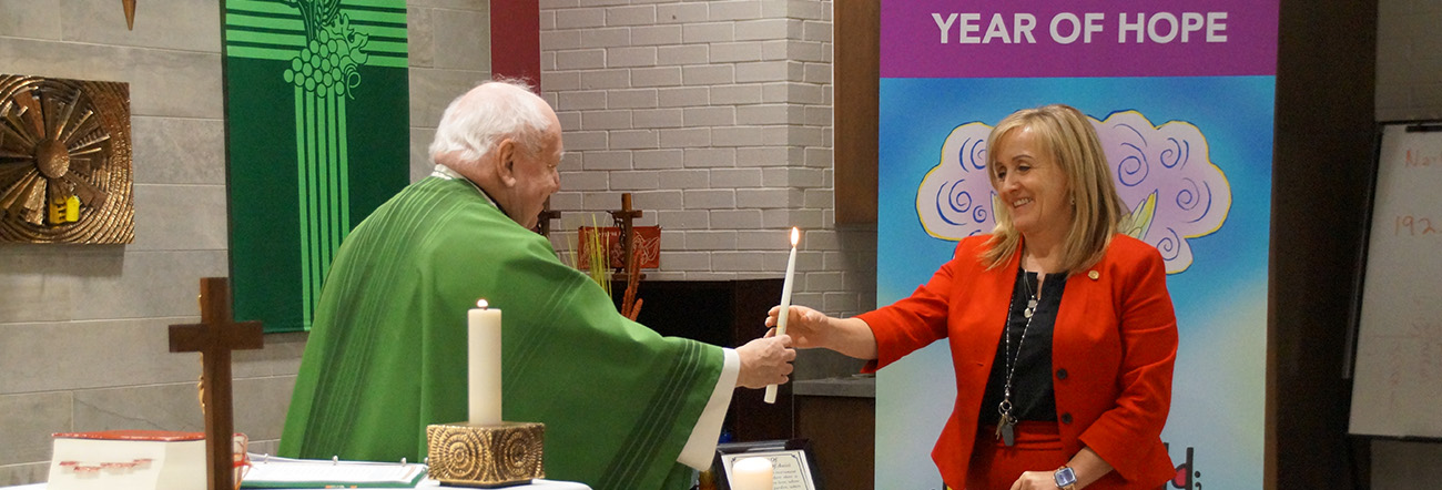 Male priest handing female adult a candle