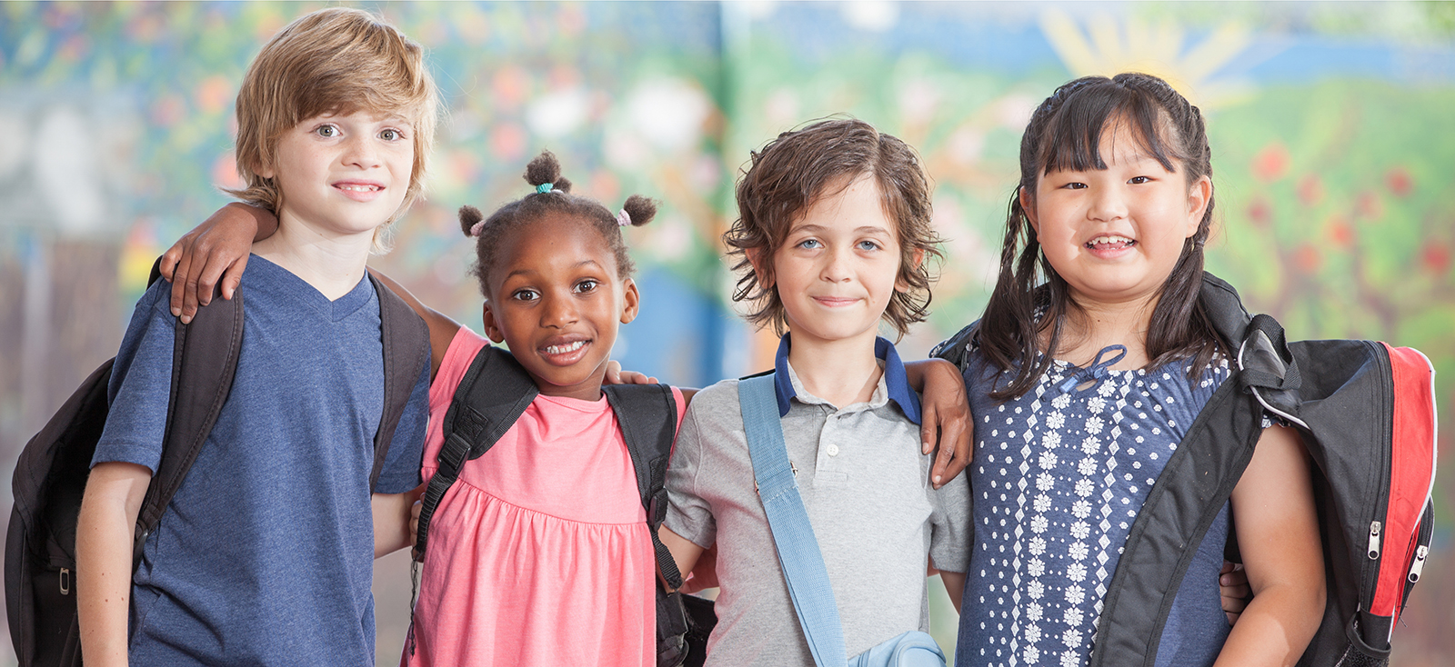 Two boys and two girls standing arm to arm with backpacks on