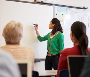 teacher at whiteboard with students in chairs