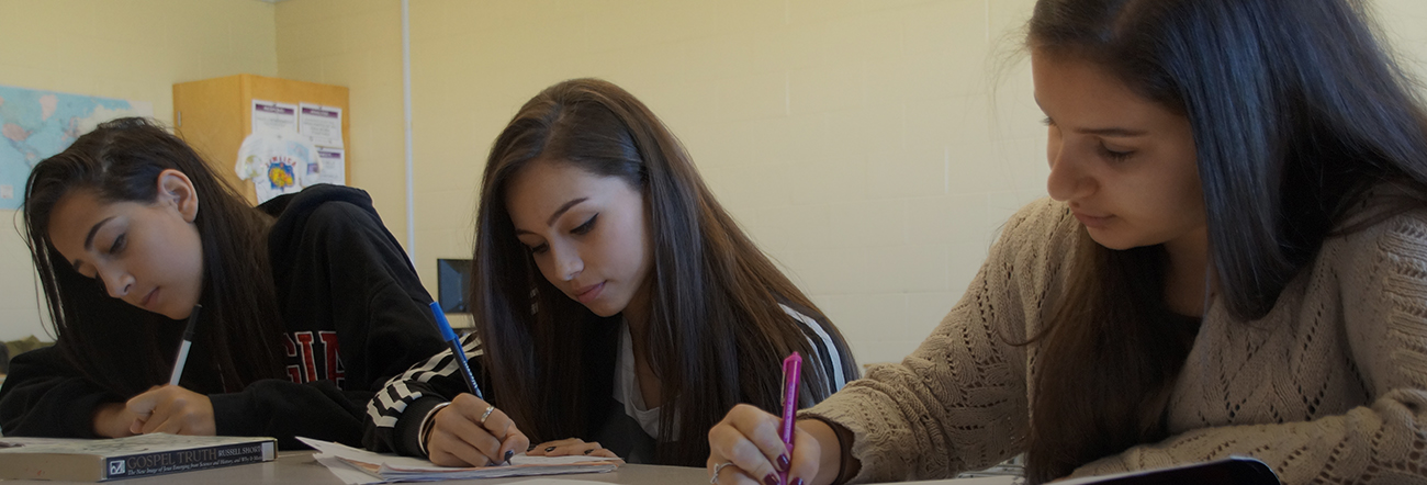 Three female students writing in a classroom